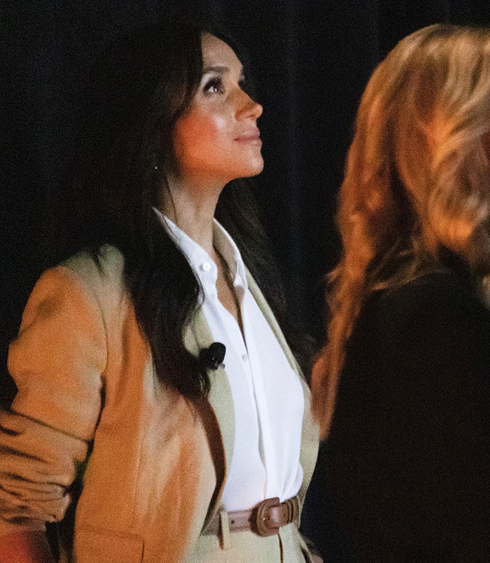 Woman in beige suit and white shirt looking upward, related to Meghan Markle backlash and Lana Del Rey's husband praised. Woman in beige suit and white shirt looking upward, related to Meghan Markle backlash and Lana Del Rey's husband praised.