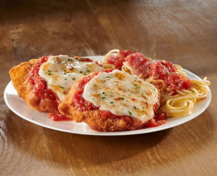 Plate of Italian chicken parmesan with melted cheese and spaghetti topped with marinara sauce representing Olive Garden dish request by American tourist.