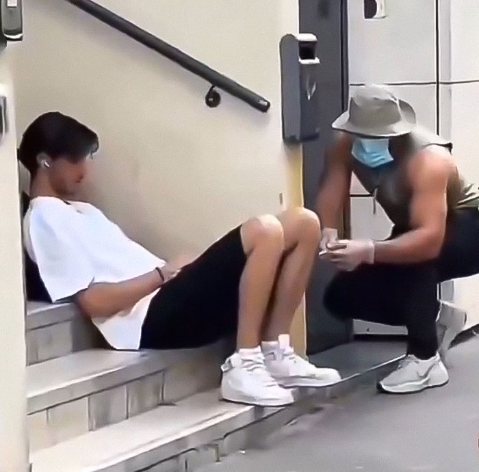 Man wearing mask and gloves holding a fake syringe near a seated young person in a prank influencer video.