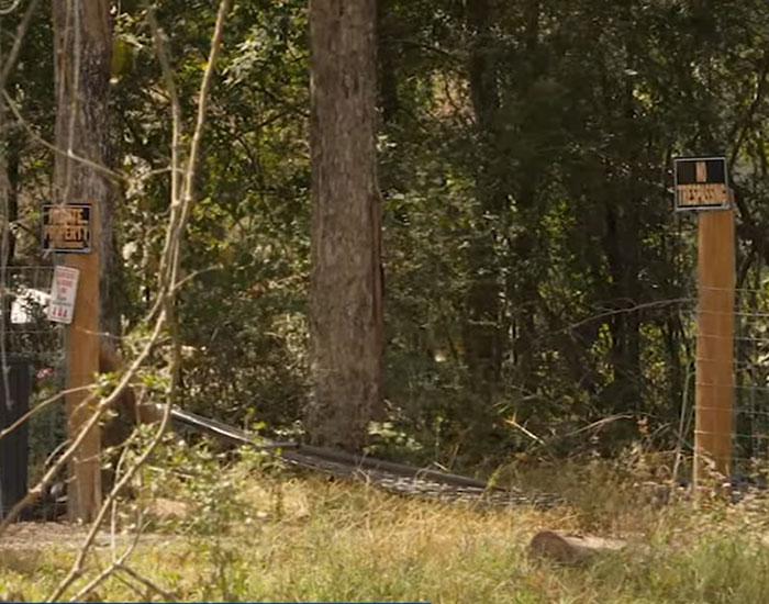 Wooded area with fence posts and multiple no trespassing signs at entrance to private property.