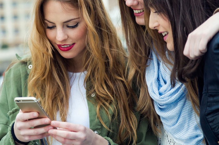 Three young women closely looking at a phone, capturing a moment of unexpected and awkward discovery.