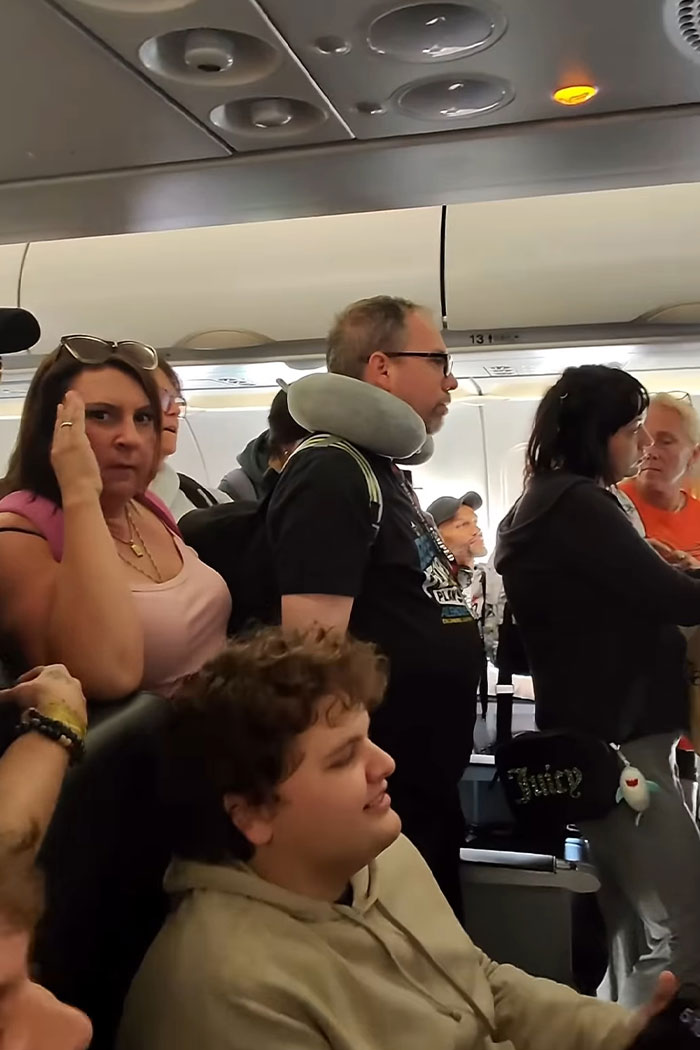 Passengers on a plane stand and wait in the aisle as a woman insufferably refuses to let others exit first. Passengers on a plane stand and wait in the aisle as a woman insufferably refuses to let others exit first.