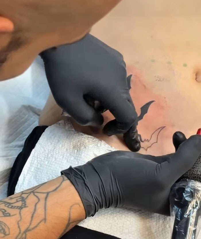 Tattoo artist wearing black gloves creating a pelvic tattoo on a young person's lower abdomen. Tattoo artist wearing black gloves creating a pelvic tattoo on a young person's lower abdomen.
