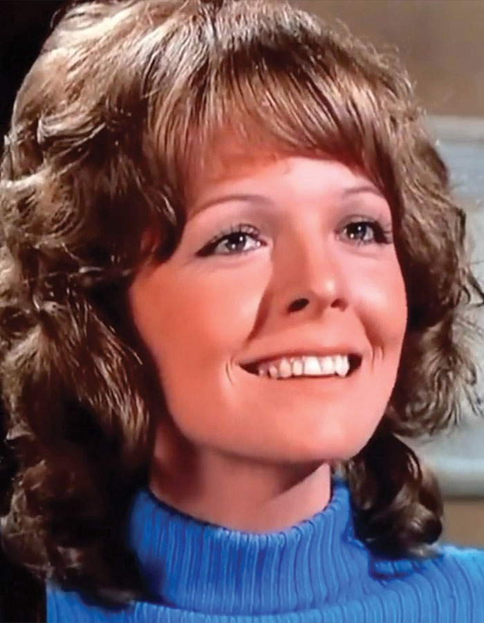 Close-up of a woman smiling with curly hair, wearing a blue turtleneck, related to Diane Keaton health and home sale.