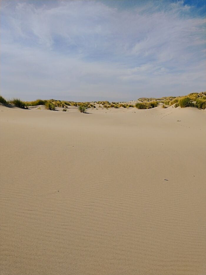 Liminal space of empty sand dunes with sparse vegetation under a partly cloudy sky evoking a beautiful yet unnerving scene