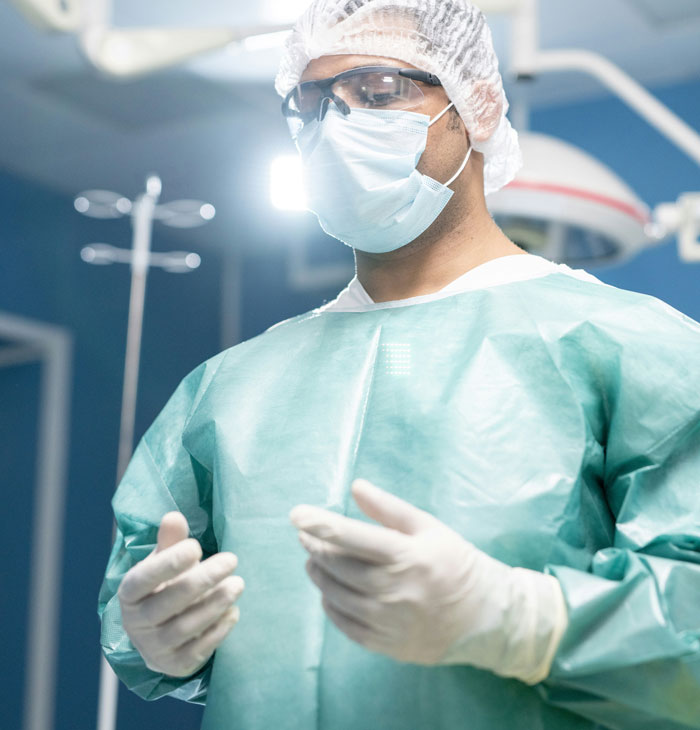 Plastic surgeon wearing protective gear and gloves preparing for surgery in a bright operating room environment.