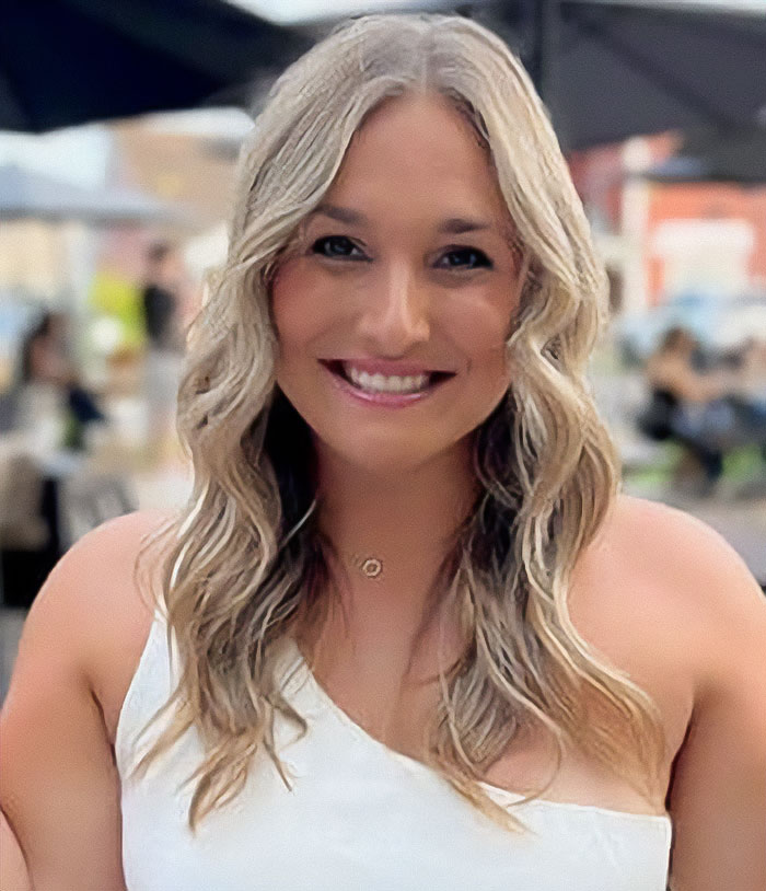 Woman with long blonde hair smiling at an outdoor caf&eacute; discussing officials revealing cause of passing of couple in car.