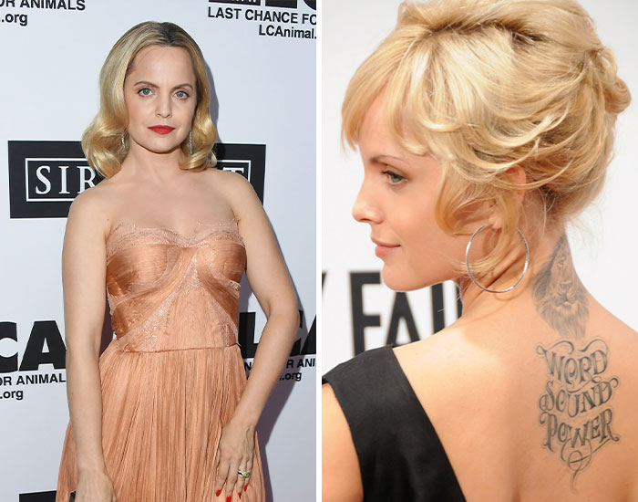 Female celebrity with blonde hair wearing a strapless dress and showing a detailed back tattoo with the phrase word sound power