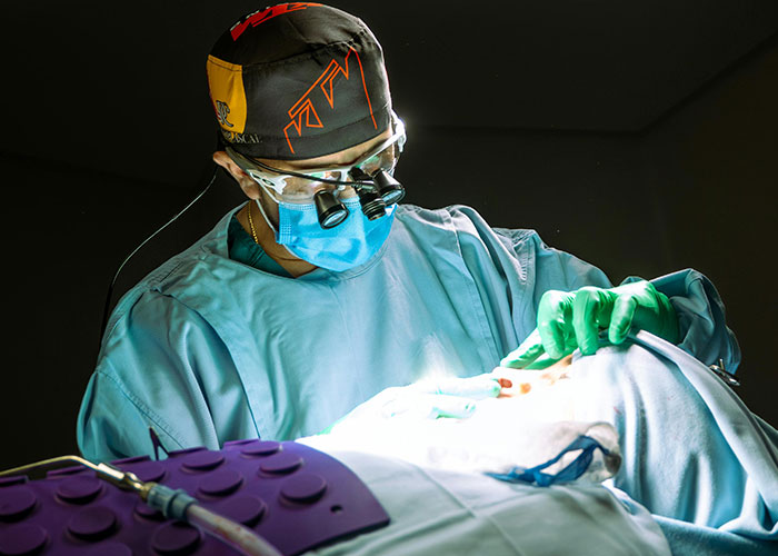 Surgeon performing a cosmetic procedure in an operating room, focused and wearing surgical gear and magnifying glasses.
