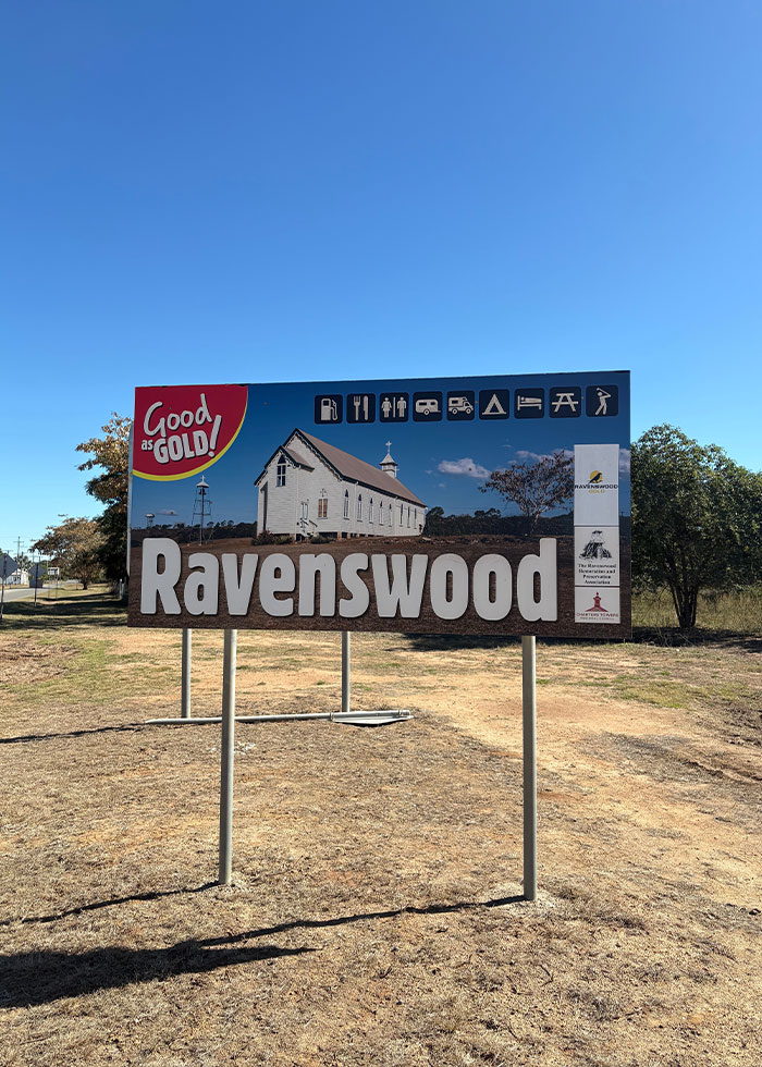 Roadside sign for Ravenswood town with a historic church under clear blue sky, related to woman knocked unconscious by bird insurance story.