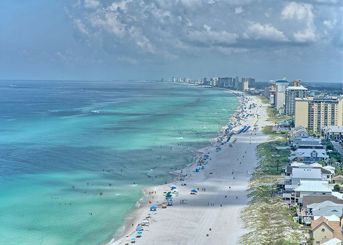 Aerial view of a crowded beach with turquoise water and buildings along the shore, highlighting mom leaving 6-month-old baby alone.