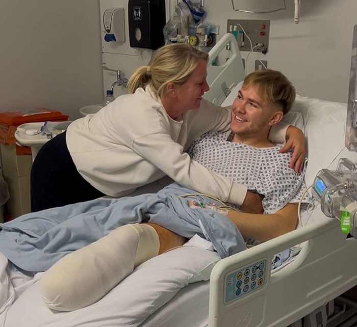 Young man with leg amputation in hospital bed smiling while a woman embraces him, sharing his recovery story.