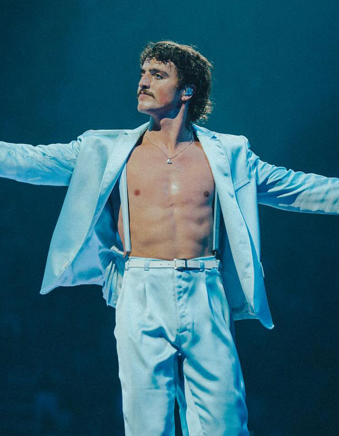 Man with mustache in open white suit and suspenders on stage, illustrating the Mormon Backflip Theory viral trend.