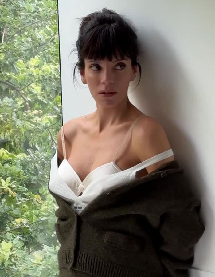 Lily Allen posing by window in a white top and dark cardigan, seemingly revealing what happened with David Harbour.