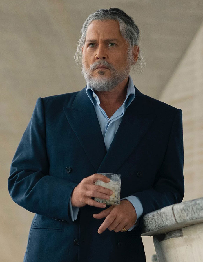 Johnny Depp in character for new movie role facing backlash, dressed in a dark suit holding a glass, serious expression.