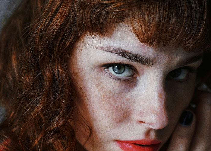 Close-up of a woman with intense blue eyes and red hair, evoking the creepy things women said or did to men.