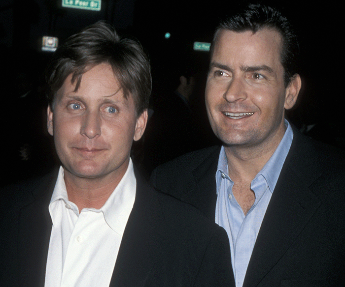 Actors Emilio Estevez and Charlie Sheen smiling together at a nighttime event, dressed in formal attire. Actors Emilio Estevez and Charlie Sheen smiling together at a nighttime event, dressed in formal attire.