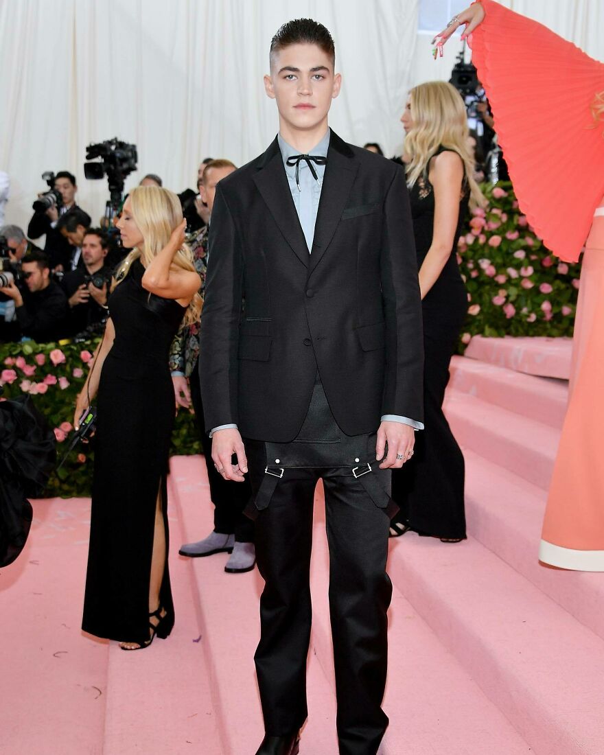 Hero Fiennes celebrity nepo baby wearing a black suit with unique pants posing on a pink carpet at a high-profile event.