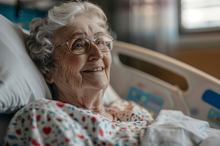 Elderly woman smiling in hospital bed wearing glasses, relating to scary ghost stories hospital work setting.
