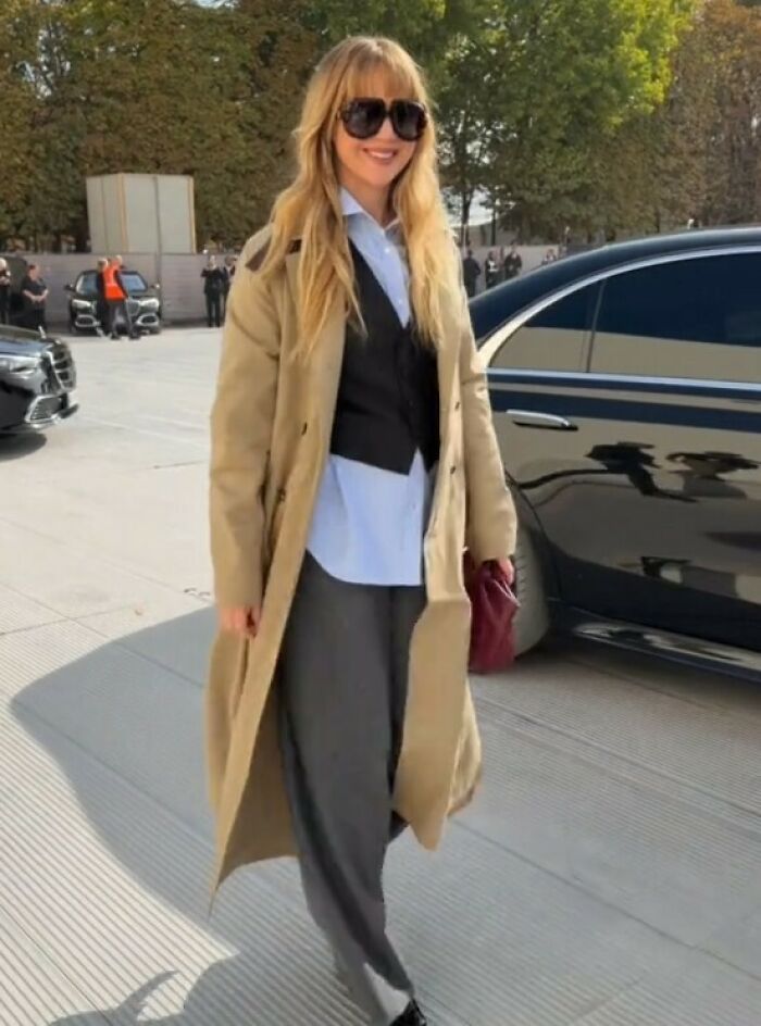 Jennifer Lawrence wearing a beige coat and sunglasses outside by luxury cars, sparking buzz on plastic surgeons in LA.