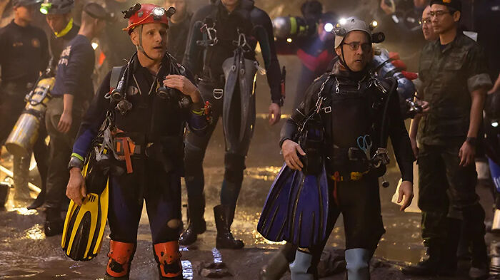 Divers in wetsuits carrying fins and equipment during a rescue operation featured in movies based on true stories.