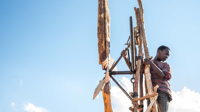 Young boy climbing a tall wooden structure outdoors in a scene from a movie based on true stories.