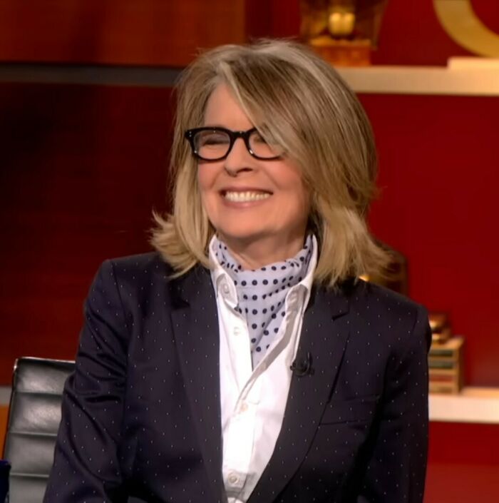 Diane Keaton smiling in glasses and polka dot scarf during a TV interview discussing unexpected passing cause.