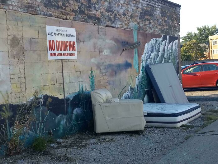 Discarded couch and mattress by a wall with a no dumping sign, illustrating people allergic to acting like sensible adults.