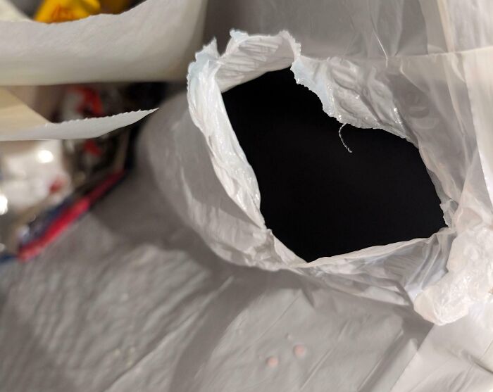 Torn plastic bag with large hole on a white textured surface, illustrating carelessness or damage.