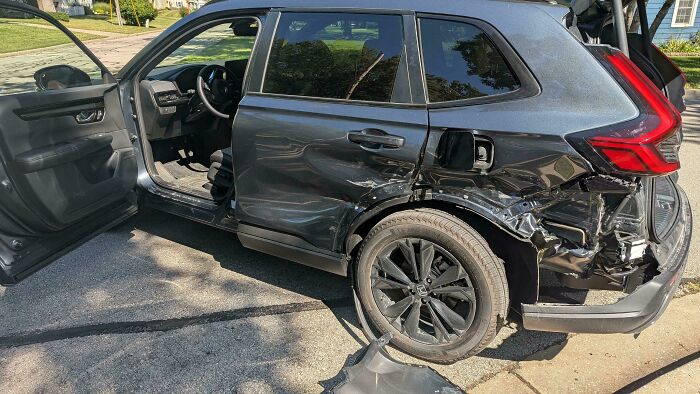 Black SUV with severe rear side damage and open front door, illustrating people apparently allergic to acting like sensible adults.