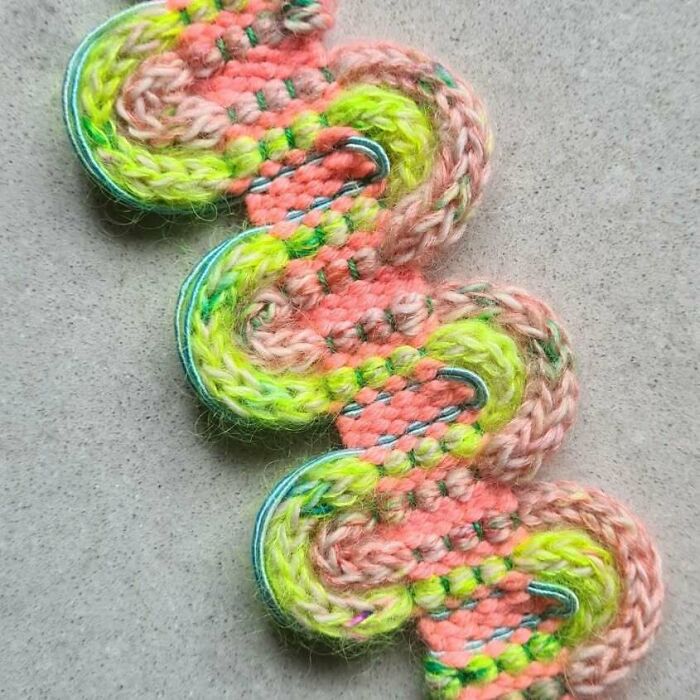 Colorful textile creation featuring vibrant threads woven in a mesmerizing zigzag pattern on a gray background.