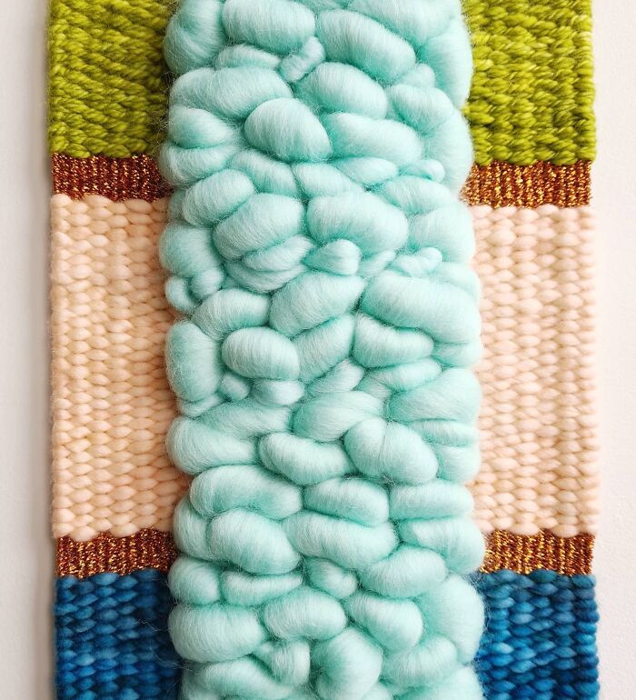 Soft textured textile creation featuring thick turquoise threads with green, peach, copper, and blue woven patterns.