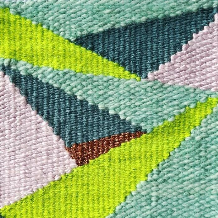 Close-up of colorful textile creation showing intricate threads woven into geometric patterns with vibrant green and pastel shades.