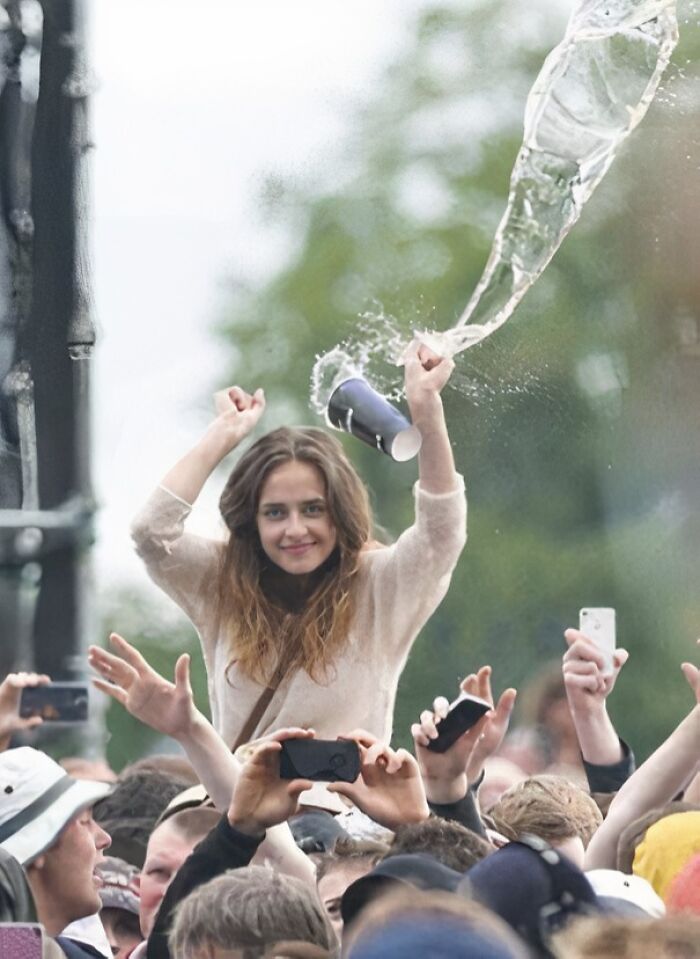 Young woman in a crowd raising hands as a cup splashes water, capturing the split second before disaster hits hilariously.