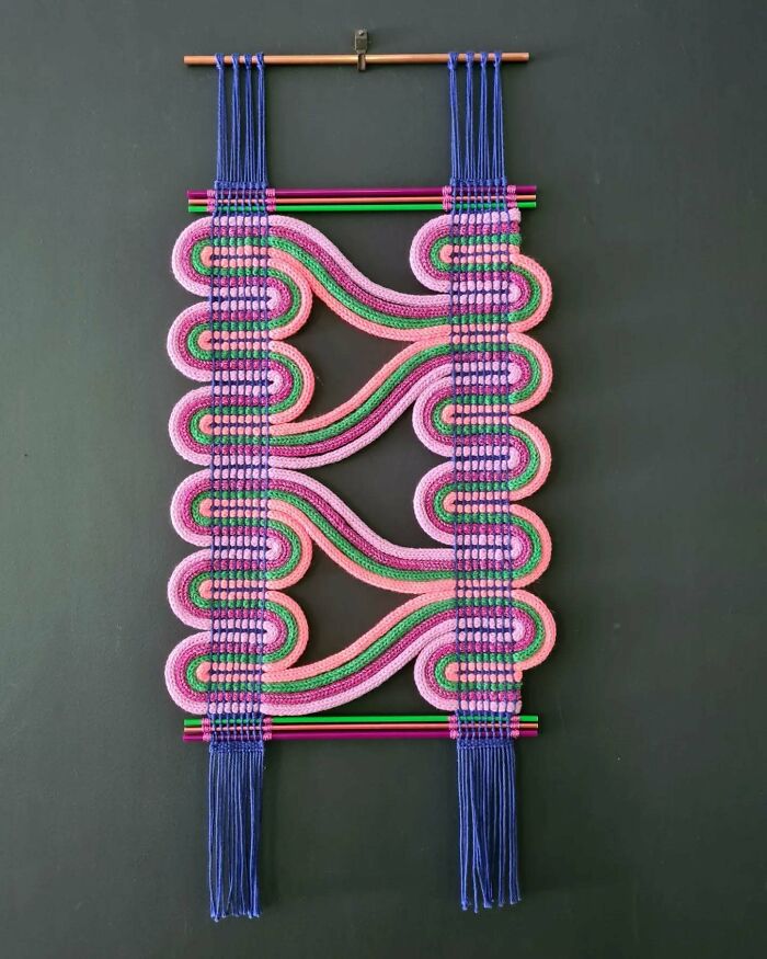Colorful textile art hanging on a wall featuring intricate threads in pink, green, and blue forming mesmerizing patterns.
