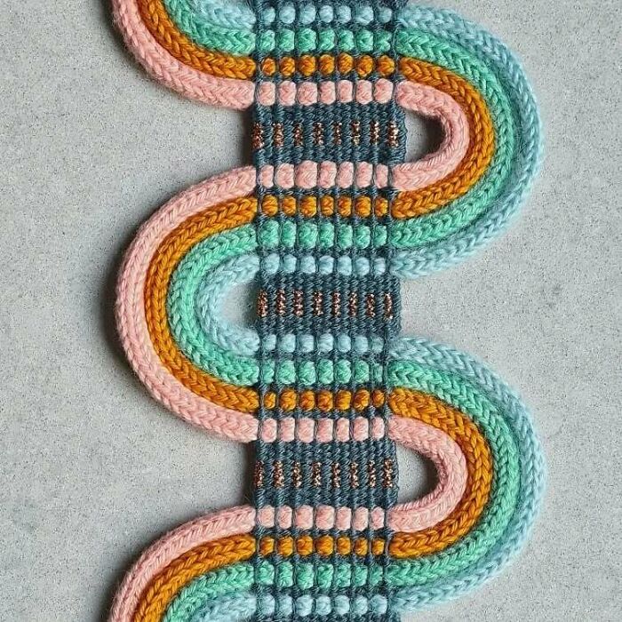 Colorful textile creation with intricate woven threads forming mesmerizing looping patterns on a gray background.