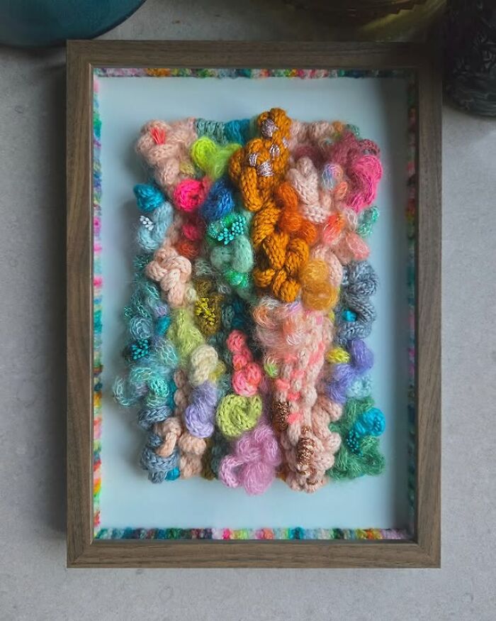 Colorful textile creation made of various textured threads displayed in a wooden frame, showcasing mesmerizing fiber art.