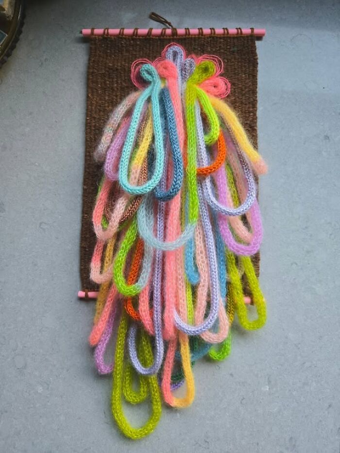 Colorful textile creation with loops of knitted threads hanging from a dark woven background, showcasing mesmerizing textile art.