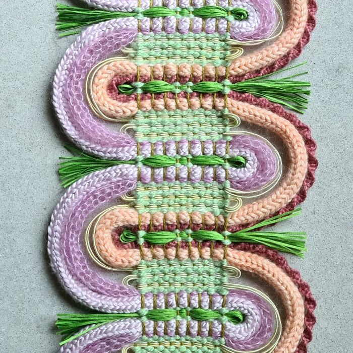 Intricate textile creation featuring colorful woven threads and green tassels in an eye-catching artistic design.