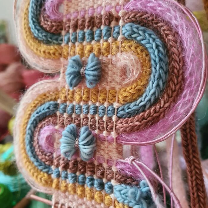 Close-up of colorful textile creation featuring intricate knitting and woven threads in pastel shades with detailed blue yarn embellishments.