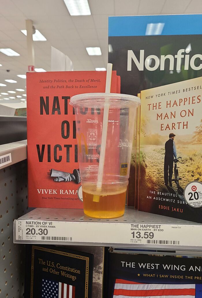 Clear plastic cup with a straw and a small amount of drink placed on a bookstore shelf among nonfiction books.
