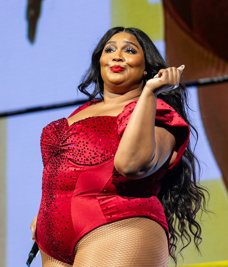 Lizzo performing on stage in a red outfit, showcasing her wellness evolution and confident stage presence.
