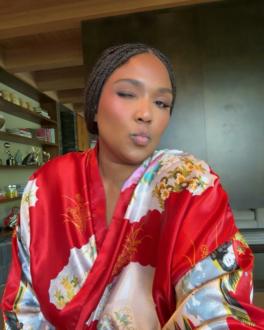 Lizzo in a colorful satin robe, winking with a playful expression, highlighting her wellness evolution and confidence.