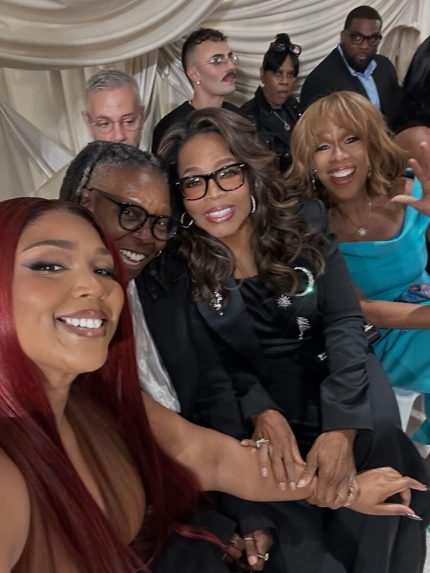 Group of smiling people posing for a casual photo showcasing Lizzo&rsquo;s wellness evolution at a social event indoors.