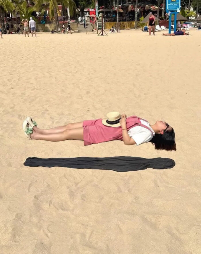 Woman lying straight on sand with a shadow that looks like a distorted extension in unphotoshopped pics that look fake but real.