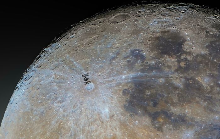 Close-up astronomy photo of the moon's surface with a space station silhouetted against the detailed lunar landscape.