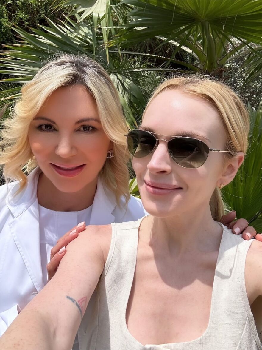 Lindsay Lohan taking a selfie outdoors with a blonde woman in white coat, showcasing evolving look and style changes.