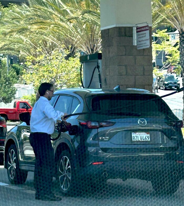 Man in casual outfit refueling black Mazda CX-5 at gas station, illustrating people allergic to acting like sensible adults.