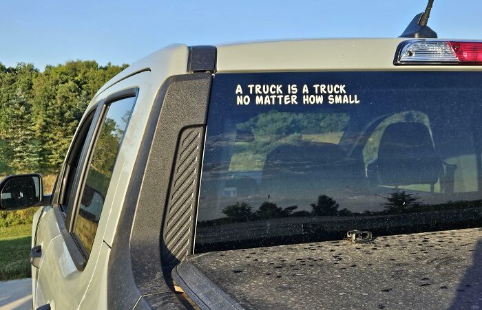 Bumper sticker on truck window reading a clever and funny message about trucks, captured on the road.