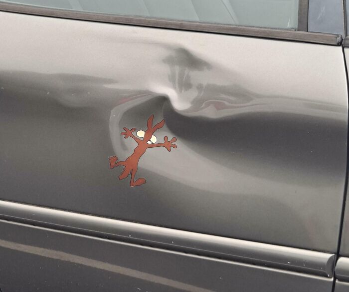 Car door dent with a clever and hilarious bumper sticker of a cartoon character stuck as if caught in the damage.